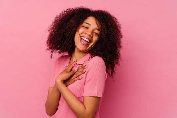 Jeune femme afro-américaine isolée sur fond rose a une expression amicale, pressant la paume sur la poitrine. Concept d'amour. - Photo, image