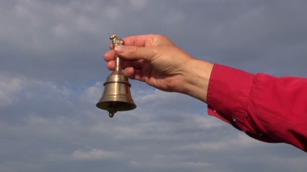 ruka drží dekorativní mosazný zvonek na pozadí modré oblohy - Záběry, video