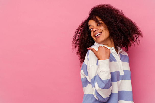 Giovane donna afroamericana isolata su punti di sfondo rosa con il pollice lontano, ridendo e spensierato. - Foto, immagini