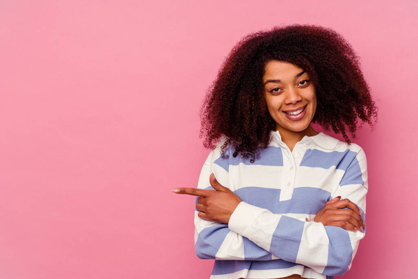 Joven mujer afroamericana aislada sobre fondo rosa sonriendo alegremente señalando con el dedo índice de distancia. - Foto, Imagen