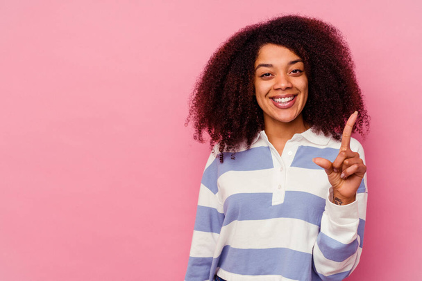 ピンクの背景に孤立した若いアフリカ系アメリカ人女性は指でナンバーワンを示す. - 写真・画像
