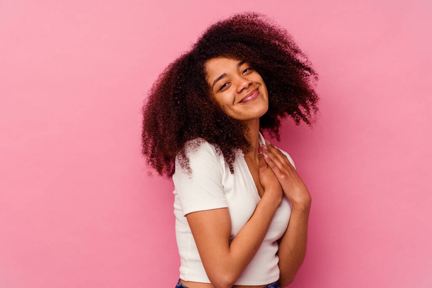 ピンクの背景に隔離された若いアフリカ系アメリカ人女性は、胸に手のひらを押して、フレンドリーな表情をしています。愛の概念. - 写真・画像