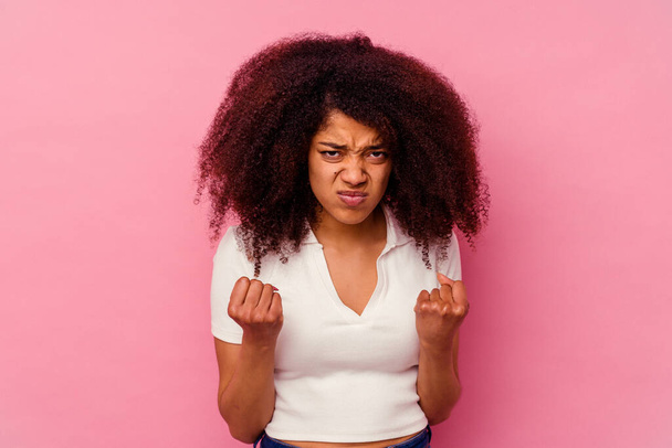 Mujer afroamericana joven aislada sobre fondo rosa mostrando puño a cámara, expresión facial agresiva. - Foto, Imagen