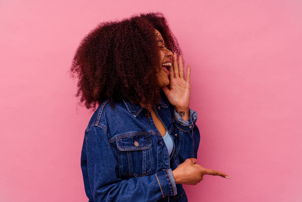 Young african american woman isolated on pink background saying a gossip, pointing to side reporting something. - Fotoğraf, Görsel