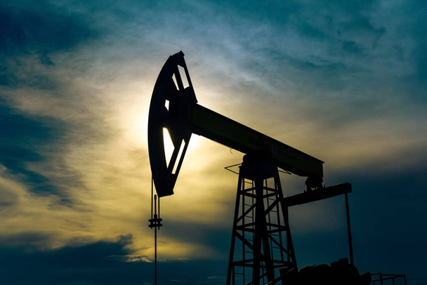 силуэт насоса с поршневым насосом на нефтяной скважине на фоне неба - Фото, изображение