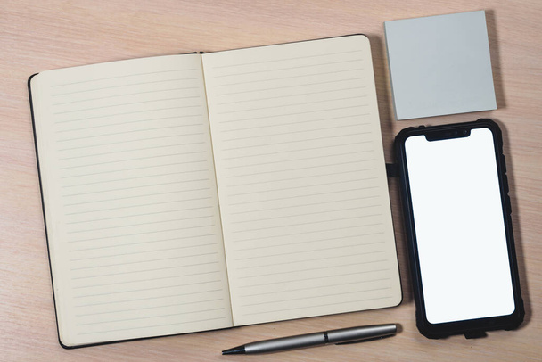Mockup image of a smartphone with the blank white screen, pen, sticky notes and a notebook on a wooden table. - Photo, image