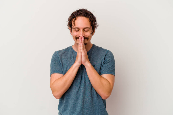 Young caucasian man isolated on white background holding hands in pray near mouth, feels confident. - Photo, Image