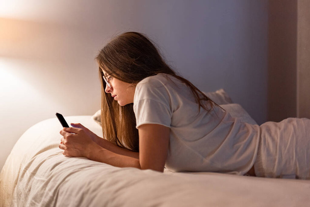 Mujer latina joven con teléfono móvil acostado en la cama - Foto, imagen