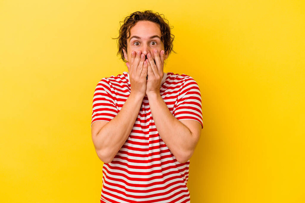 Young caucasian man isolated on yellow background shocked, covering mouth with hands, anxious to discover something new. - Photo, Image