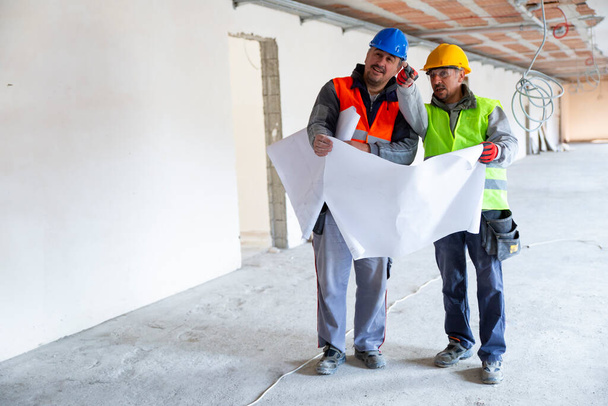 Ingénieurs pointant le mur avec un plan directeur sur le chantier de construction - Photo, image
