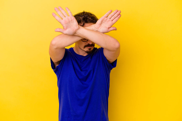 Young caucasian man isolated on yellow background keeping two arms crossed, denial concept. - Photo, Image