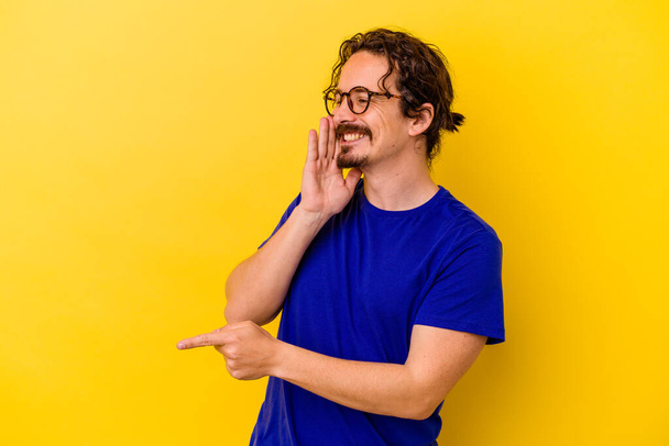 Young caucasian man isolated on yellow background saying a gossip, pointing to side reporting something. - Photo, Image