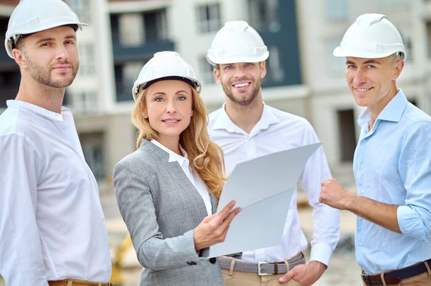 Confident building inspector with a document and builders looking ahead - Valokuva, kuva