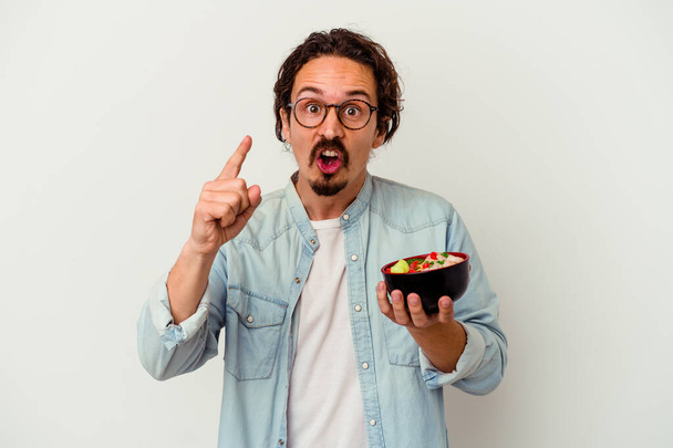 Молодий білий чоловік їсть рамен, ізольований на білому тлі, має ідею, концепцію натхнення
. - Фото, зображення