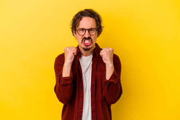 Young caucasian man isolated on yellow background upset screaming with tense hands. - Photo, Image