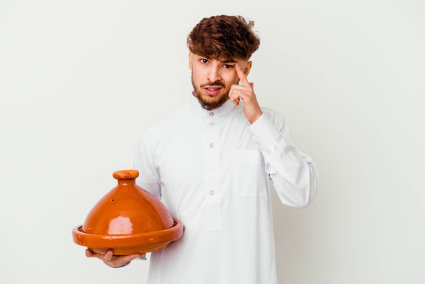 Jonge Marokkaanse man draagt de typische Arabische kostuum met een tajine geïsoleerd op witte achtergrond toont een teleurstelling gebaar met wijsvinger. - Foto, afbeelding