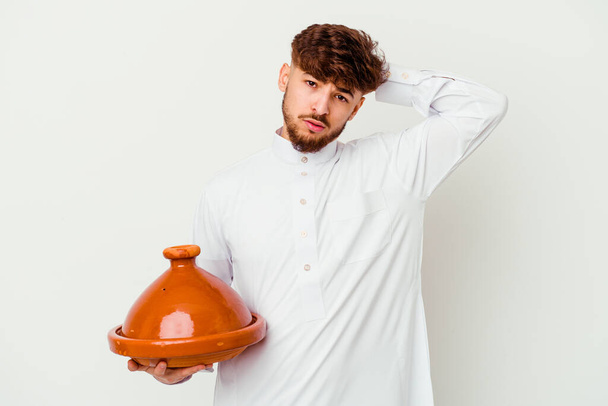 Junge marokkanische Mann in der typischen arabischen Tracht hält eine Tajine isoliert auf weißem Hintergrund schockiert, hat sie wichtige Treffen erinnert. - Foto, Bild