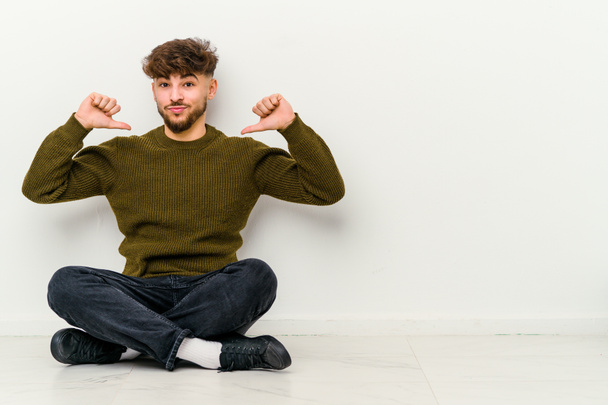 Young Moroccan man sitting on the floor isolated on white background feels proud and self confident, example to follow. - Photo, Image