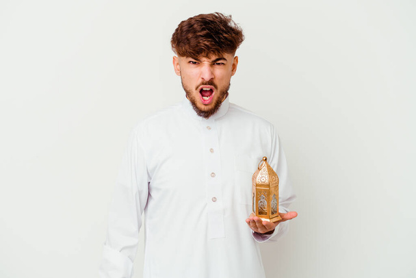 白い背景に隔離されたラマダーンランプを持っている典型的なアラブの服を着ている若いモロッコの男は非常に怒って積極的に叫んで. - 写真・画像
