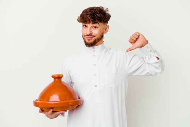 Joven hombre marroquí con el típico traje árabe sosteniendo un tajine aislado sobre fondo blanco se siente orgulloso y seguro de sí mismo, ejemplo a seguir. - Foto, imagen