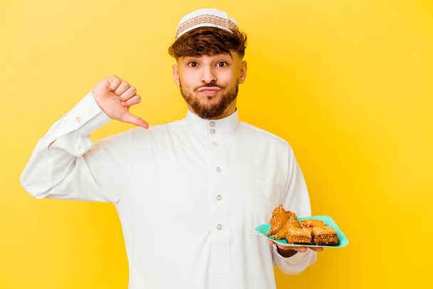 Mladý Maročan v typickém arabském kostýmu jíst arabské sladkosti izolované na žlutém pozadí cítí hrdost a sebevědomí, příklad následovat. - Fotografie, Obrázek
