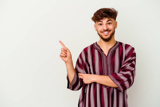 Joven hombre marroquí aislado sobre fondo blanco sonriendo alegremente señalando con el dedo índice de distancia. - Foto, imagen