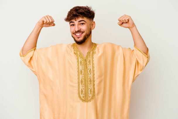 白い背景に孤立した若いモロッコ人男性は、女性の力の象徴である腕を持つ強さのジェスチャーを示しています。 - 写真・画像