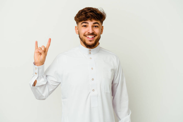 Молодой марокканский мужчина в типичной арабской одежде на белом фоне показывает жест рога как революционная концепция. - Фото, изображение