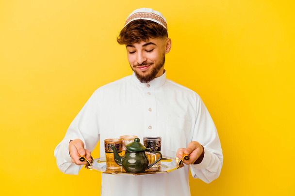 若いですモロッコ人男性身に着けています典型的なアラビア語の衣装黄色の背景に隔離されたお茶を飲む - 写真・画像