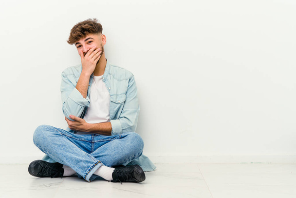 Young Moroccan man sitting on the floor isolated on white background laughing happy, carefree, natural emotion. - Photo, Image