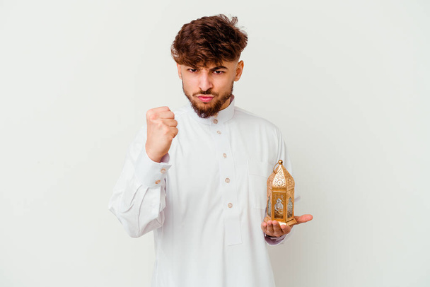 Fiatal marokkói férfi visel tipikus arab ruhát tartó ramadán lámpa elszigetelt fehér háttér mutatja ököllel a kamera, agresszív arckifejezés. - Fotó, kép