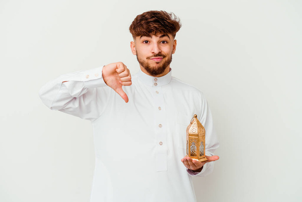 Jovem marroquino vestindo uma roupa típica árabe segurando uma lâmpada ramadã isolada no fundo branco mostrando um gesto de antipatia, polegares para baixo. Conceito de desacordo. - Foto, Imagem