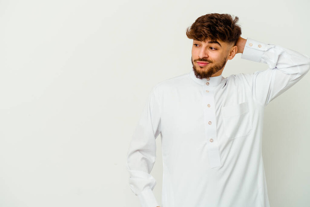 Beyaz arka planda izole edilmiş tipik bir Arap kıyafeti giyen genç Faslı adam kafasının arkasına dokunuyor, düşünüyor ve bir seçim yapıyor.. - Fotoğraf, Görsel