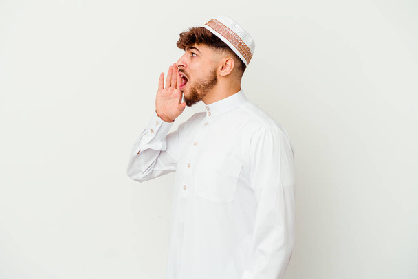 Joven árabe vestido con el típico traje árabe aislado sobre fondo blanco gritando y sosteniendo la palma cerca de la boca abierta. - Foto, imagen