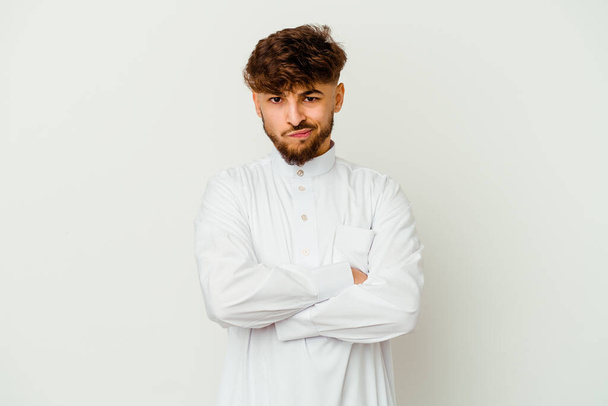 Молодой марокканский мужчина в типичной арабской одежде изолирован на белом фоне хмурясь лицо в неудовольствие, держит руки сложенными. - Фото, изображение