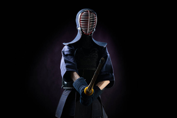 Kendo fighter in armor practicing with bamboo sword with bokuto on black background. Sports uniform - Фото, зображення