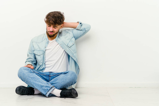 Mladý Maročan sedí na podlaze izolované na bílém pozadí s bolestí krku v důsledku stresu, masírování a dotýkání rukou. - Fotografie, Obrázek