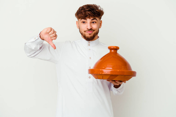 Nuorella marokkolaisella miehellä oli yllään arabialainen puku, jossa oli valkoisella pohjalla eristetty tajine, joka osoitti vastenmielisyyttä ja peukaloita alaspäin. Erimielisyyden käsite. - Valokuva, kuva