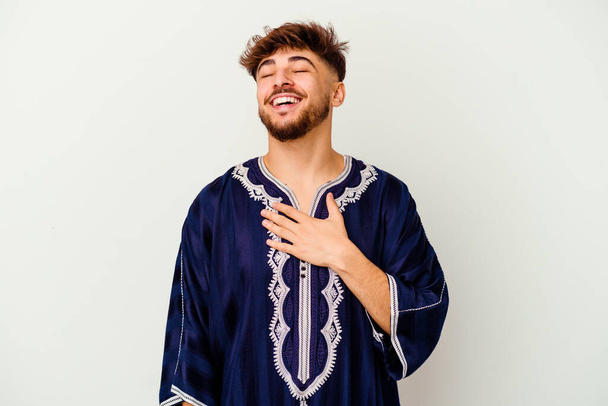 Молодой марокканский человек, изолированный на белом фоне, громко смеется, держа руку на груди. - Фото, изображение