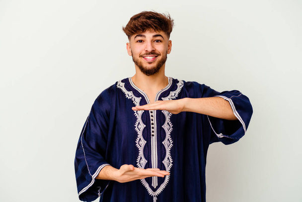 Νεαρός Μαροκινός απομονωμένος σε λευκό φόντο κρατώντας κάτι και με τα δύο χέρια, παρουσίαση προϊόντων. - Φωτογραφία, εικόνα