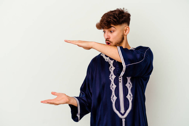 Jonge Marokkaanse man geïsoleerd op witte achtergrond geschokt en verbaasd met een kopieerruimte tussen de handen. - Foto, afbeelding