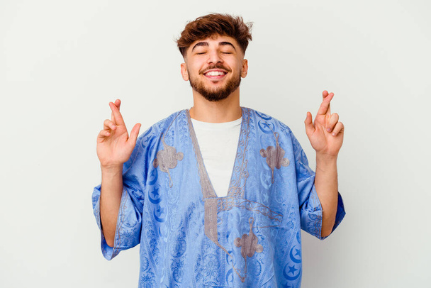 Joven hombre marroquí aislado sobre fondo blanco cruzando dedos para tener suerte - Foto, Imagen