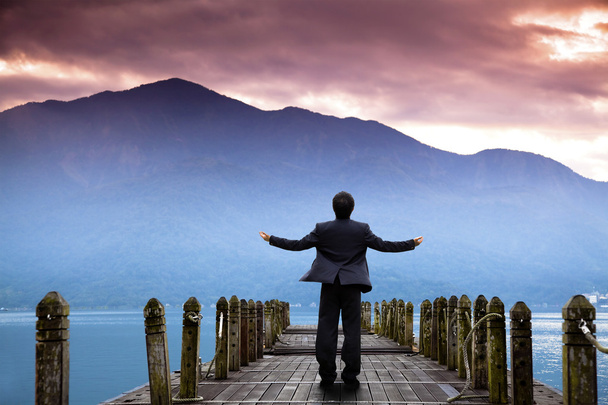 zakenman stand op de pier en kijken naar de berg en de wolk van zonsopgang - Foto, afbeelding