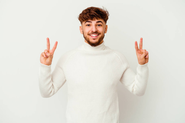 Nuori marokkolainen mies eristyksissä valkoisella taustalla osoittaa voiton merkki ja hymyilee laajasti. - Valokuva, kuva