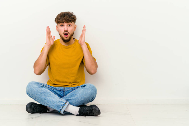 Young Moroccan man sitting on the floor isolated on white background surprised and shocked. - Photo, Image