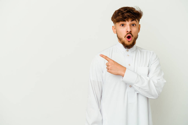 Mladý marocký muž nosí typické arabské oblečení izolované na bílém pozadí ukazuje do strany - Fotografie, Obrázek