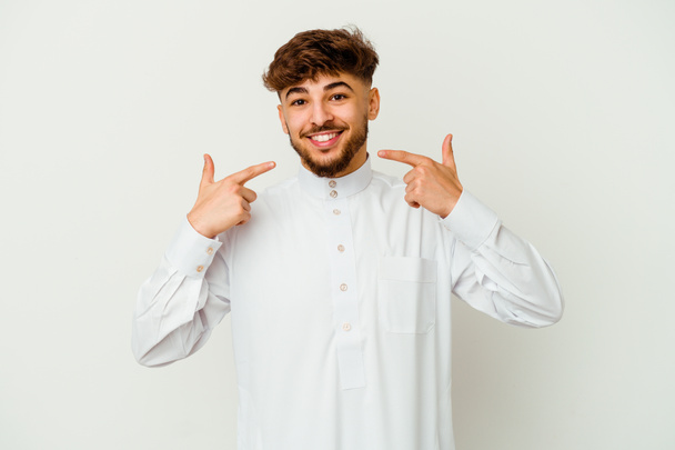 Junger marokkanischer Mann in typisch arabischer Kleidung auf weißem Hintergrund lächelt und zeigt mit den Fingern auf den Mund. - Foto, Bild
