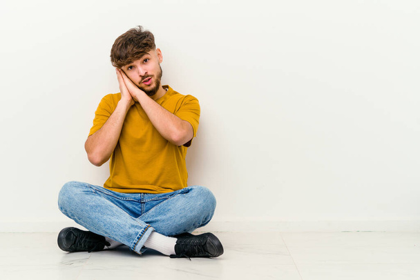 Young Moroccan man sitting on the floor isolated on white background yawning showing a tired gesture covering mouth with hand. - Photo, Image