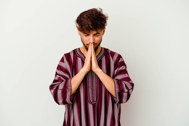 Young Moroccan man isolated on white background holding hands in pray near mouth, feels confident. - Photo, Image