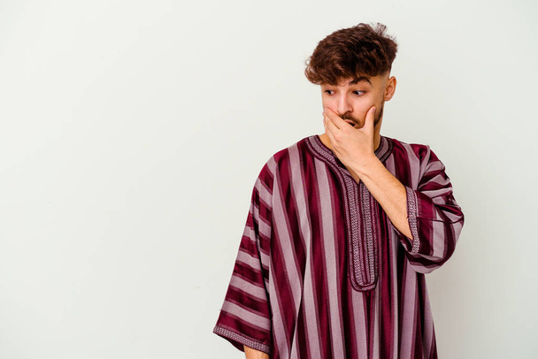 Junger marokkanischer Mann isoliert auf weißem Hintergrund, nachdenklich auf einen Kopierraum blickend, der Mund mit der Hand bedeckt. - Foto, Bild